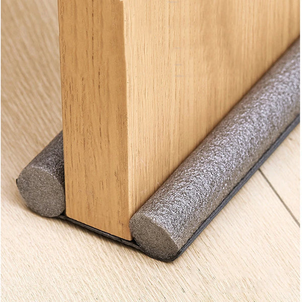 A close-up view of a wooden door frame with a gray flexible seal strip installed at the bottom to prevent drafts.