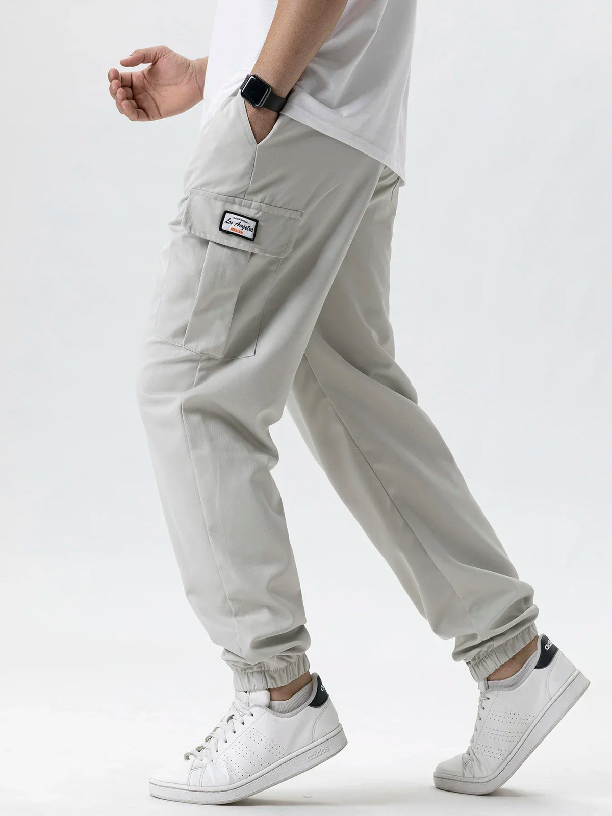 A man wearing light gray cargo joggers and a white shirt, showing the fit of the adjustable waist pants.