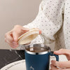 A hand holds a dark blue stainless steel insulated travel mug with a handle against a light background.
