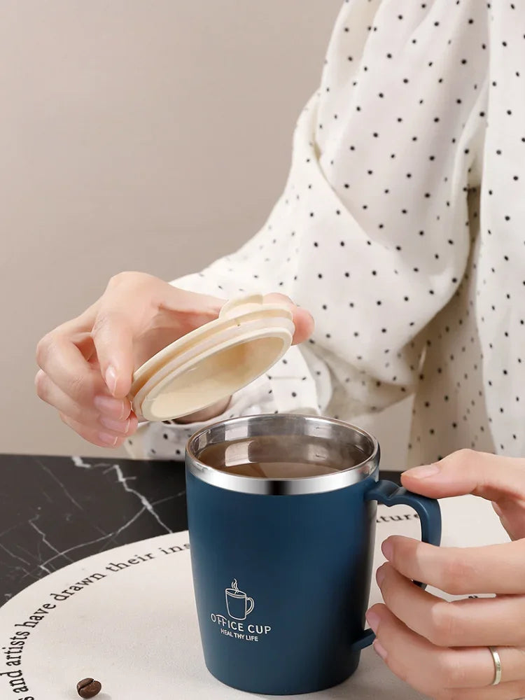 A hand holds a dark blue stainless steel insulated travel mug with a handle against a light background.