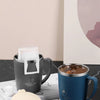 A blue stainless steel insulated travel mug is shown next to a white lid and a light-colored coaster on a dark surface.