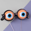 A pair of novelty glasses with large, exaggerated blue and white eyes set against a purple background.