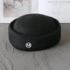 Black knitted pillbox sun hat with a wide brim resting on a gray surface.
