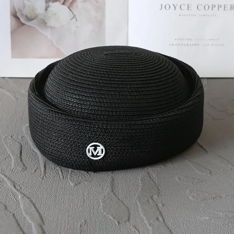 Black knitted pillbox sun hat with a wide brim resting on a gray surface.