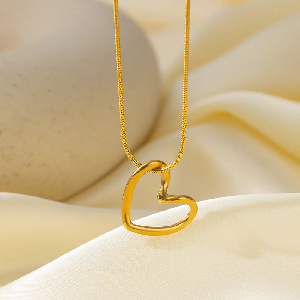A dainty gold heart pendant necklace with a snake chain resting on soft yellow fabric.