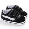 A pair of black and white striped canvas baby sneakers with anti-slip soles shown from the side.