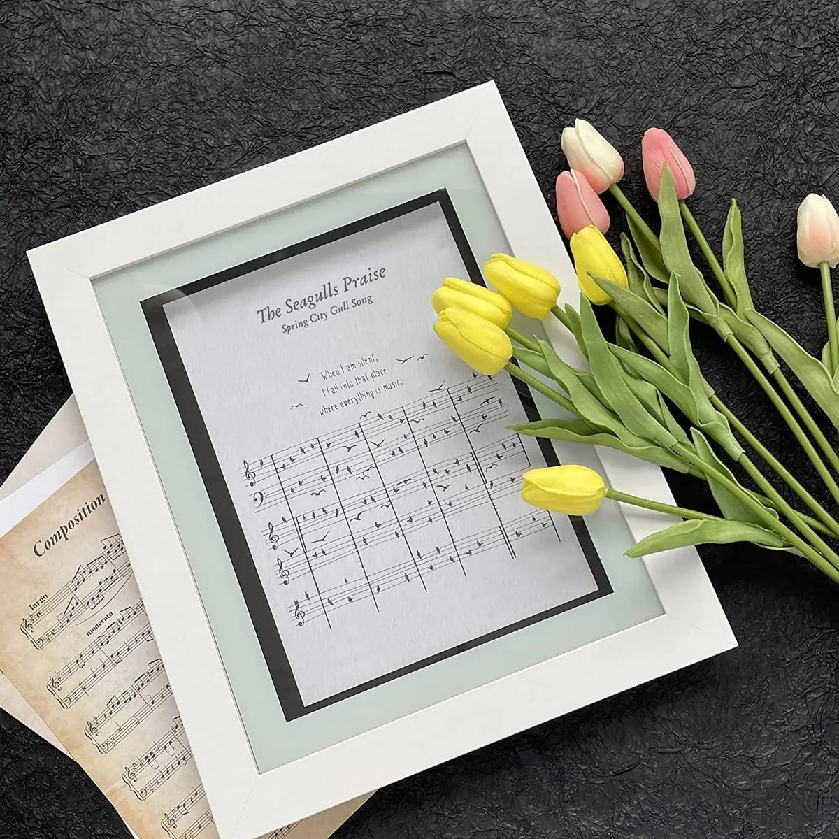 Innrammet noteark med Måkenes lovsang om vårbyen, ved siden av friske tulipaner.
