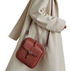 A woman holds a dusty rose vegan leather messenger bag with a leather strap against a light beige coat.