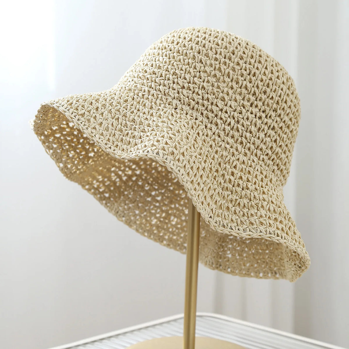 A beige crochet straw fisherman hat with a wide brim displayed on a stand.