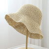 A beige crochet straw fisherman hat with a wide brim displayed on a stand.