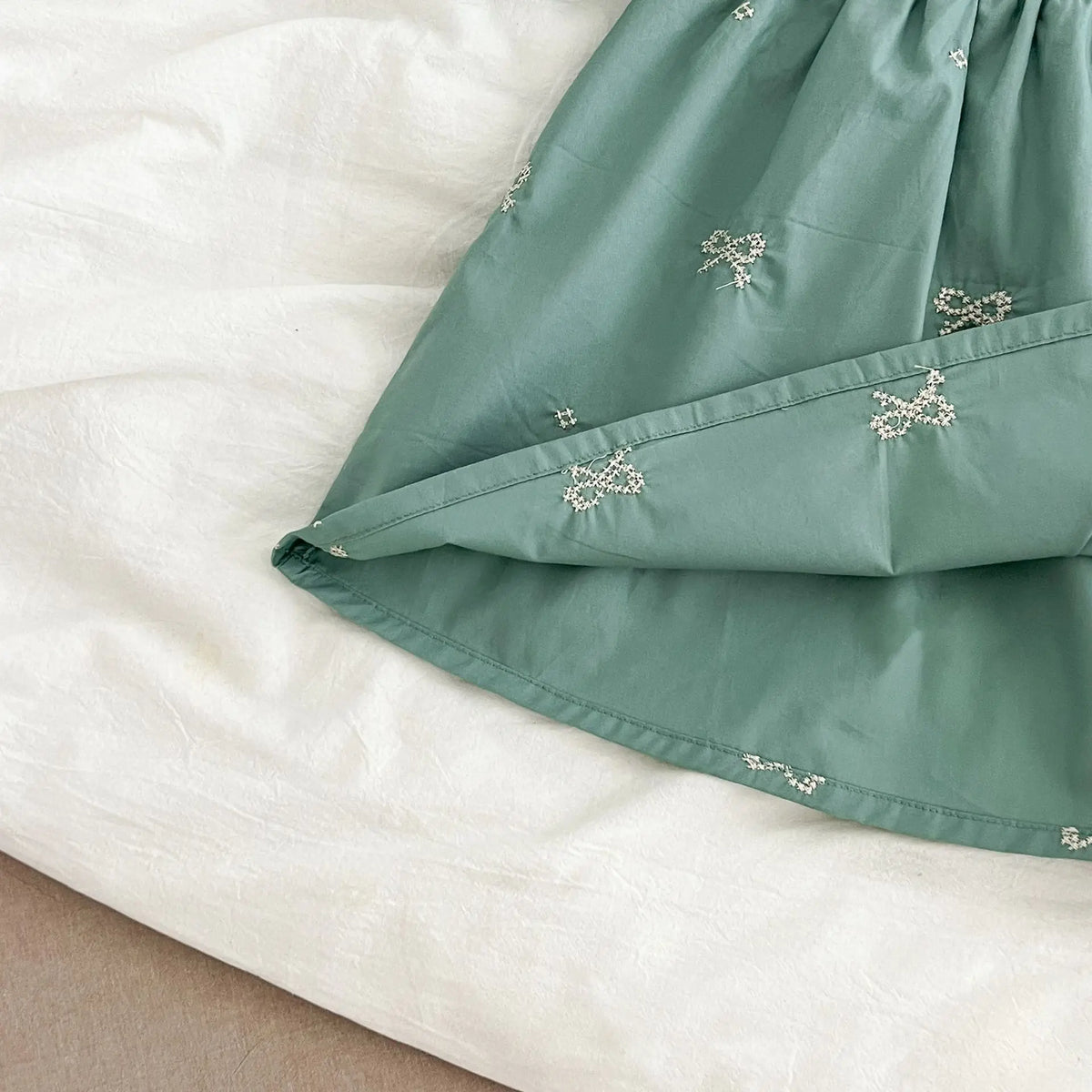 A light sage green kids princess dress with floral embroidery and lace trim folded on a white surface.