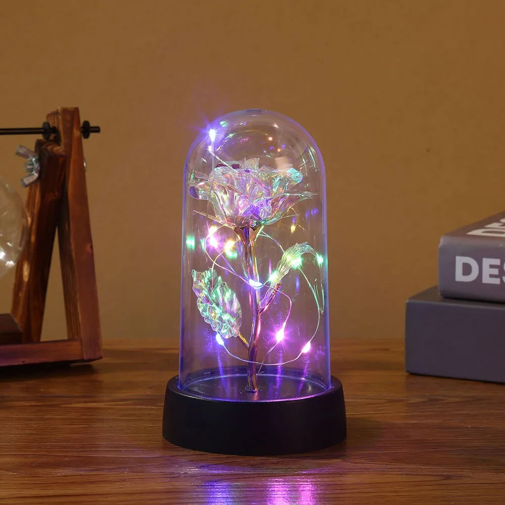 En fortryllet galakserose med LED-feelys inni en glasskuppel på en mørk overflate.