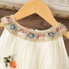 A white sleeveless dress for a baby girl featuring floral embroidery around the neckline.