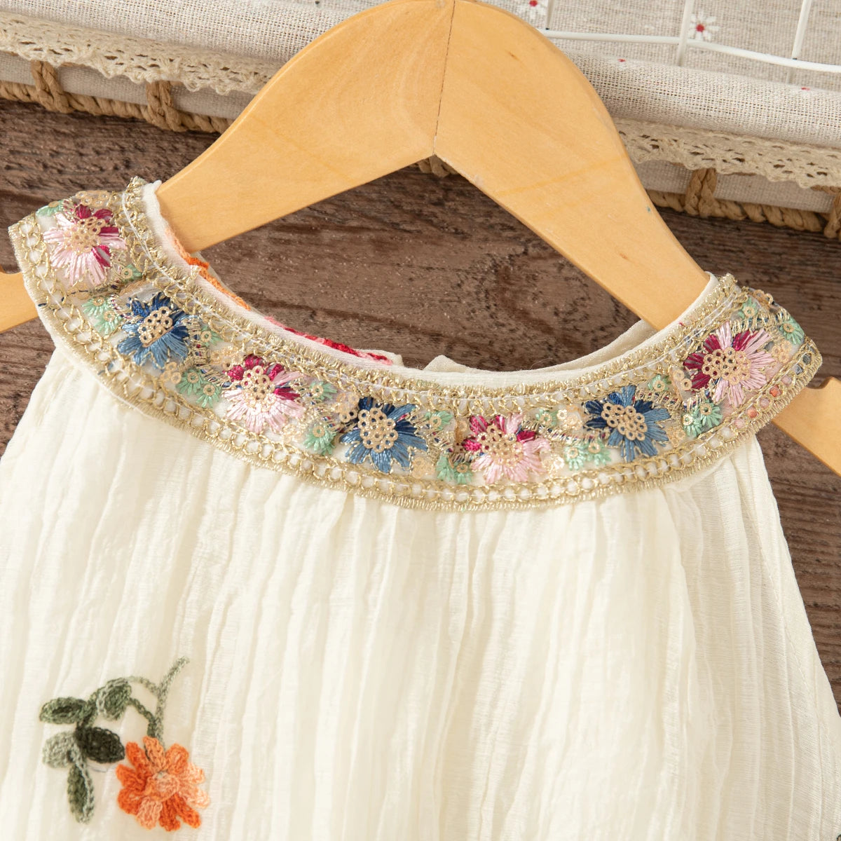 A white sleeveless dress for a baby girl featuring floral embroidery around the neckline.