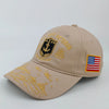 En beige militärmössa med broderad skölddesign och guldbokstäver, samt en amerikansk flagga.
