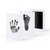 A set of white framed prints showing a handprint and a footprint in black ink on white paper.