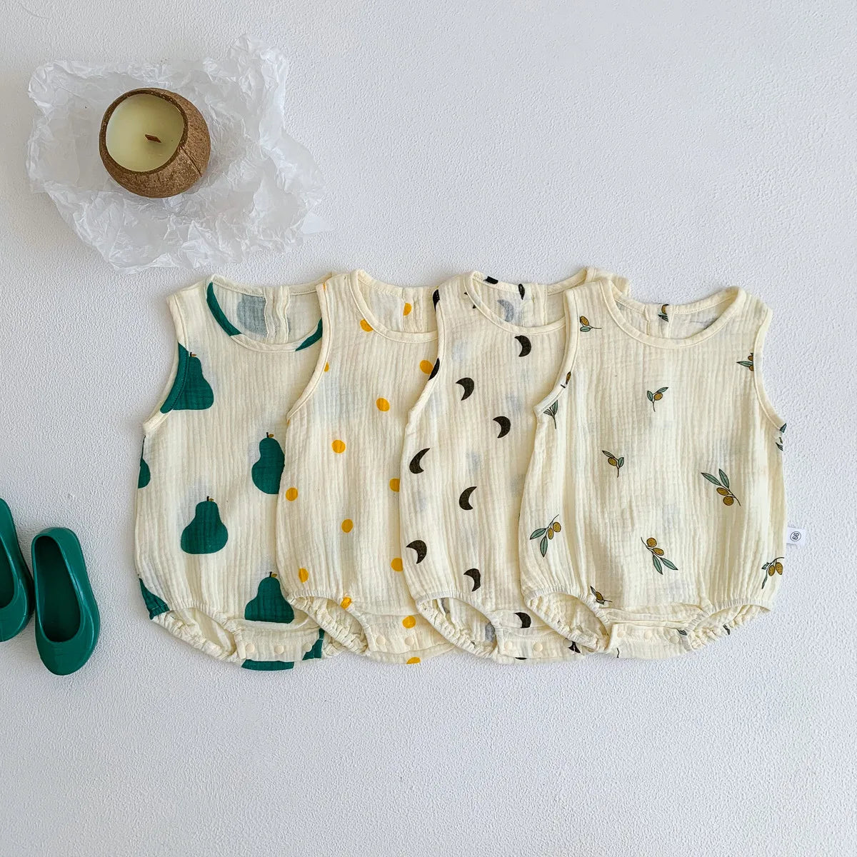 A set of five cream-colored baby cotton sleeveless jumpsuits with green and yellow leaf patterns.