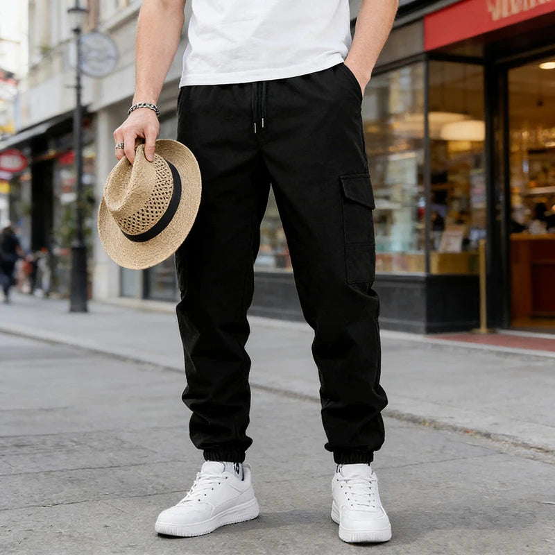 A man wearing black casual cargo pants and white sneakers stands on a sidewalk in front of a storefront.