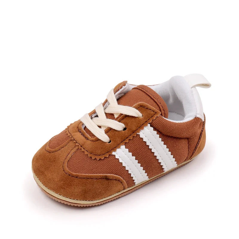 A pair of brown suede baby first walker shoes with white stripes and a white sole.