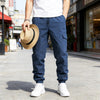 A man wearing dark blue casual cargo pants with a drawstring waist and multi-pockets standing on a sidewalk.