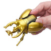 A hand holds a gold-colored wind-up insect toy, resembling a ladybug or bee, against a white background.