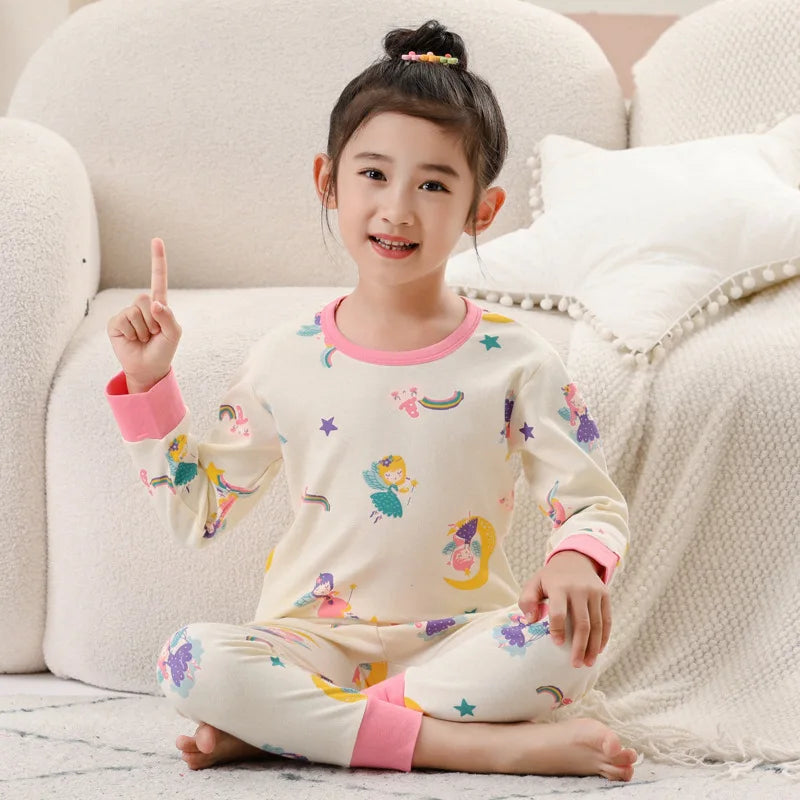 A smiling young girl wearing a cream-colored long-sleeved pajama set with colorful embroidery and pink accents.