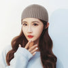 A woman wearing a beige knitted beanie and light blue sweater looking directly at the camera.