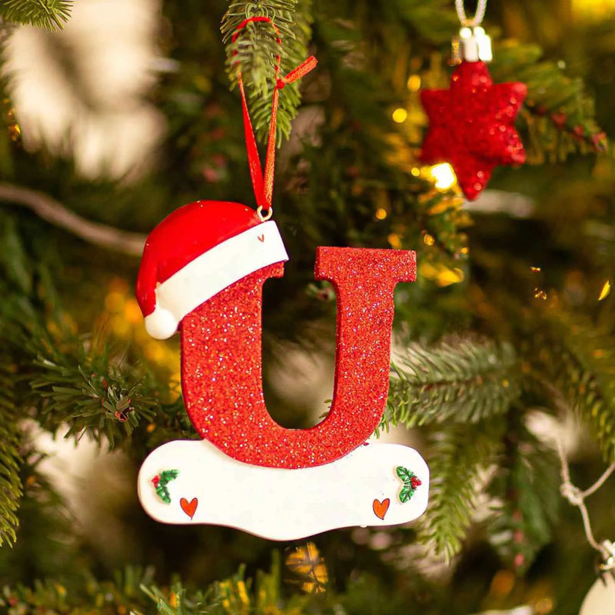 En rød og hvit akrylbokstavpynt i form av bokstaven U hengende på et juletre.