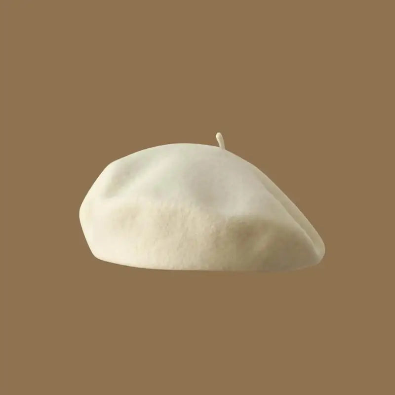 A soft, cream-colored wool beret hat viewed from the side against a brown background.