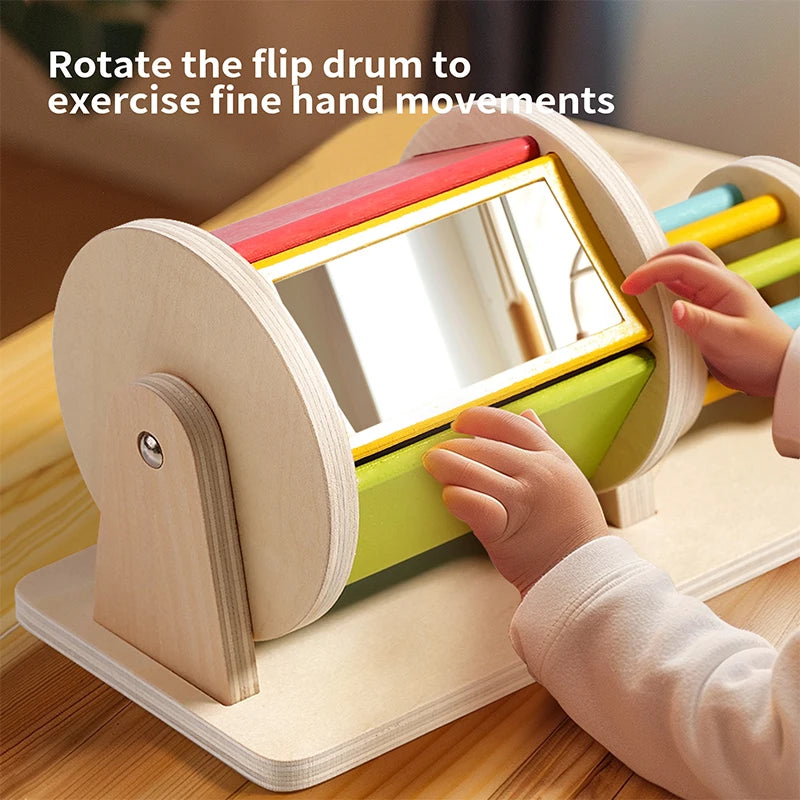 A child rotates a wooden flip drum with a mirror inside to exercise fine hand movements.