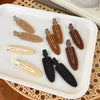 A set of matte resin side hair clips in various earth tones, including beige, brown, and black, displayed on a white tray.