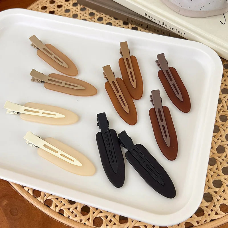A set of matte resin side hair clips in various earth tones, including beige, brown, and black, displayed on a white tray.