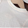 A close-up of a light beige girls cotton lace hem short sleeve tee displayed on a wooden hanger.