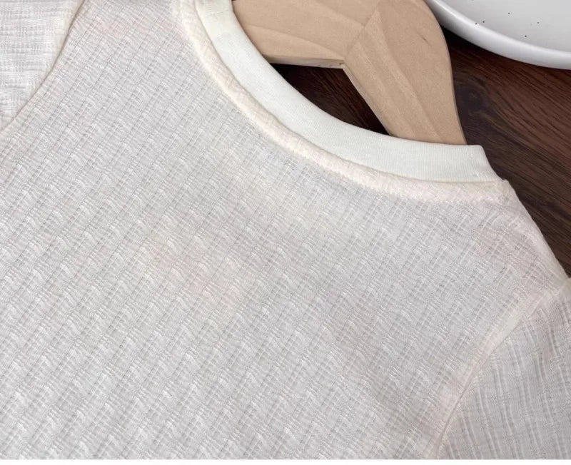 A close-up of a light beige girls cotton lace hem short sleeve tee displayed on a wooden hanger.