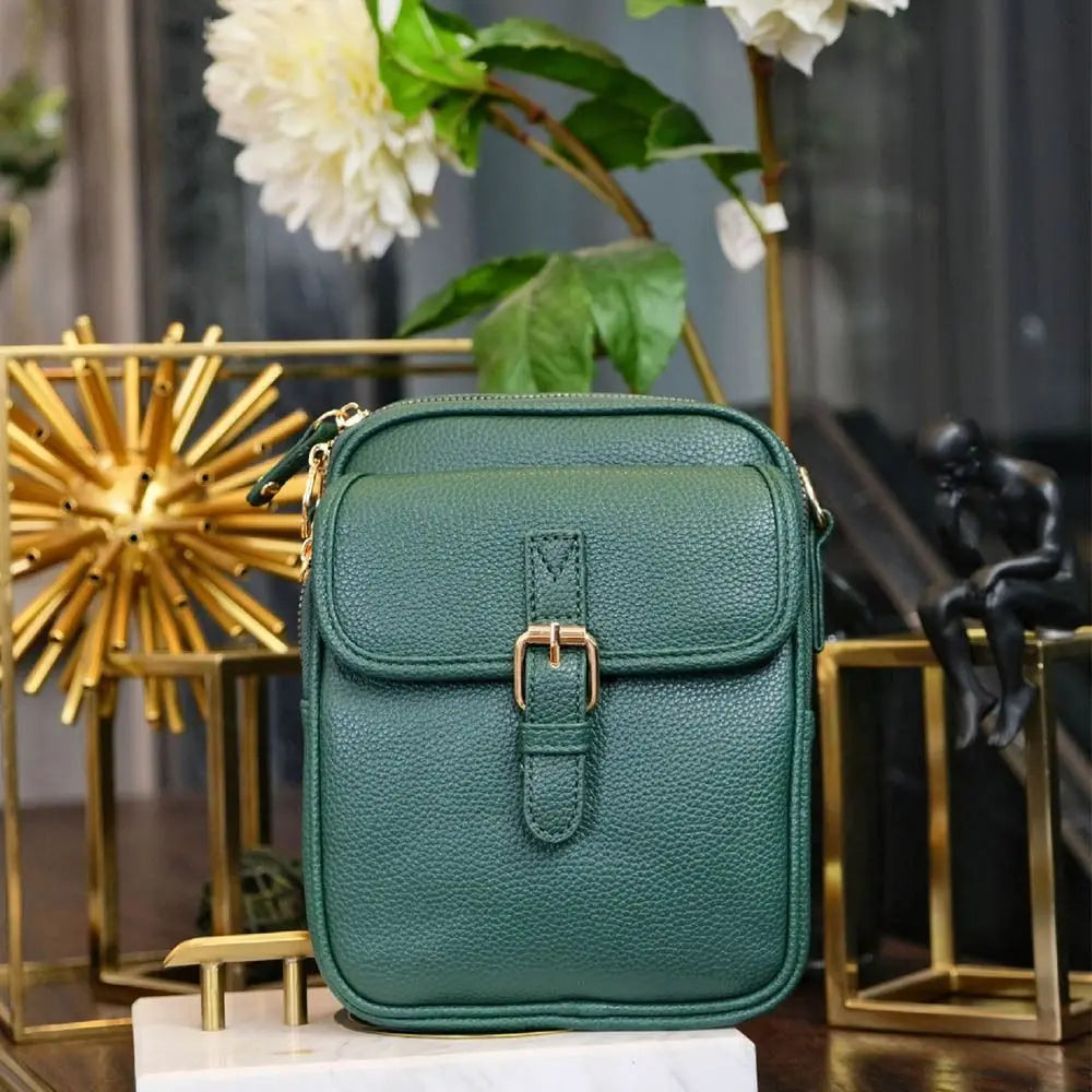 A dark green vegan leather messenger bag with gold hardware displayed on a wooden surface.