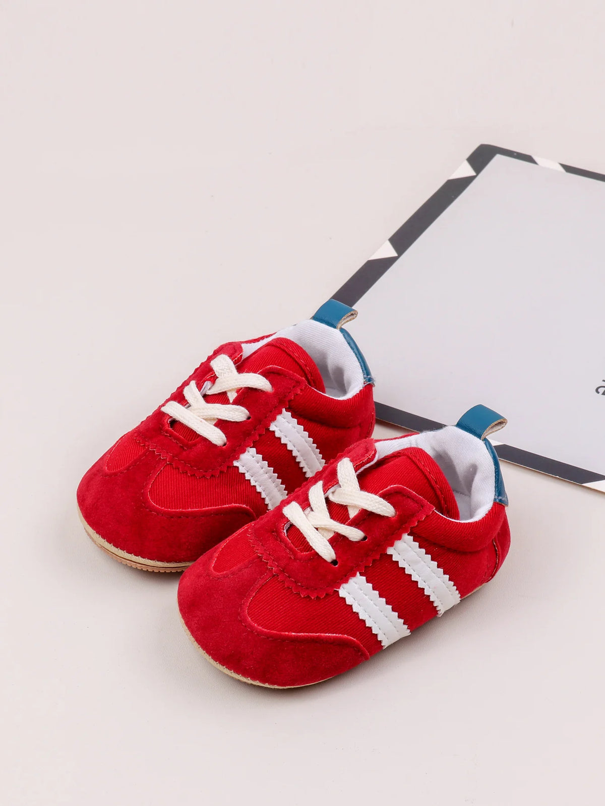 A pair of red baby first walker shoes with white laces and a sole, resting on a white background next to a card.