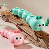 A colorful wind up worm toy and a pink reptile toy are displayed on a piece of wood.
