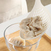 A white strainer spoon holds several translucent dumplings in a glass bowl on a wooden board.