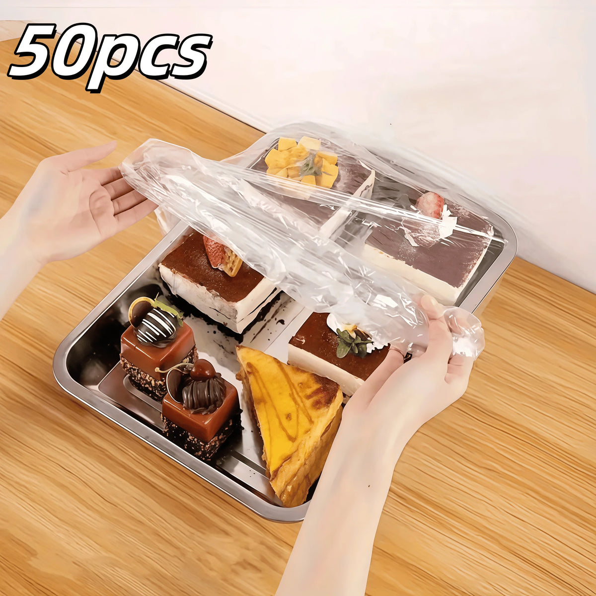 A hand is lifting a clear elastic food cover from a tray containing various baked goods and produce items.