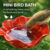 A bird is drinking water from a small, handcrafted red metal flower garden bird bath.