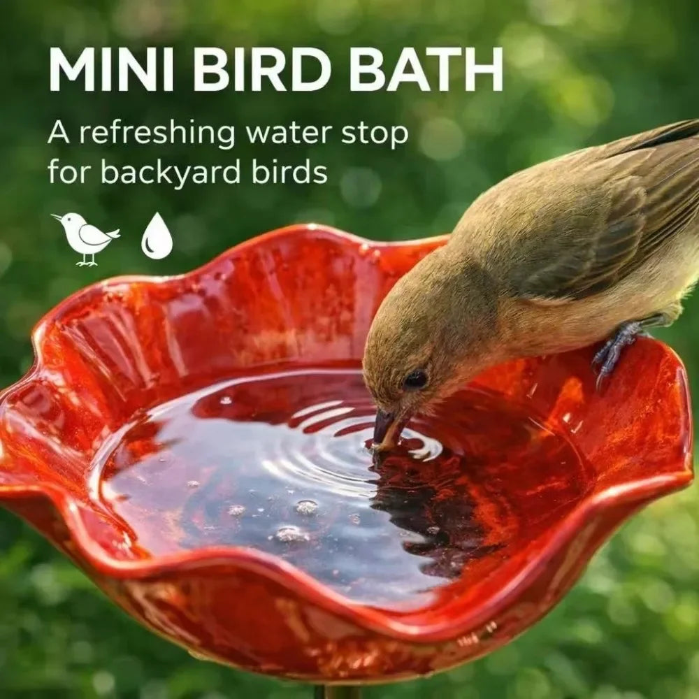 A bird is drinking water from a small, handcrafted red metal flower garden bird bath.