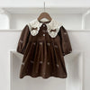 A brown kids princess dress with white lace trim and floral embroidery hanging on a wooden hanger against a white shelf.