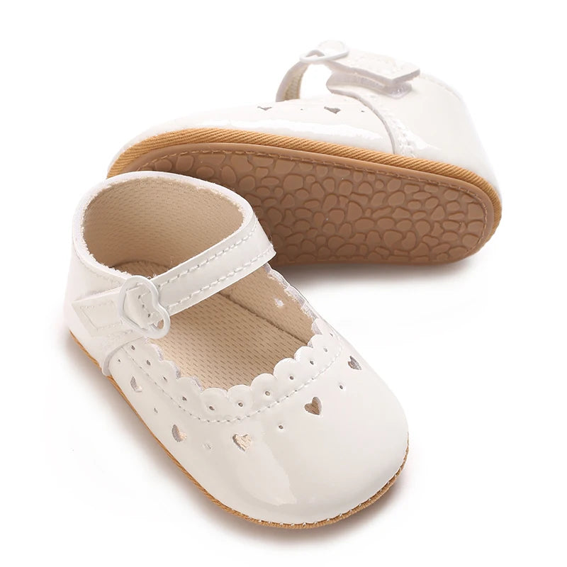 A pair of white baby first walker shoes with a textured sole and decorative cutouts on the toe.
