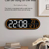A black digital wall clock displaying the time 22:08, date, and temperature, mounted on a light gray wall.