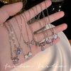 A hand displays a collection of silver and iridescent crystal bow angel wings heart pendant necklaces.