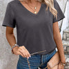 Kvinde i mørkegrå V-hals t-shirt og denimshorts med guldhalskæder og armbånd.