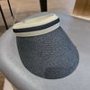 A dark gray woven straw sun hat with a light beige band resting on a gray table.