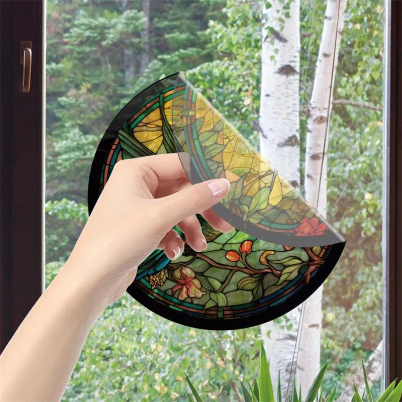 En hand håller en dekalkal med glasmosaik som föreställer en kolibri och blommor, mot en suddig utomhusbakgrund.