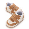 A pair of tan and white soft sole baby pre-walker sneakers for infants.