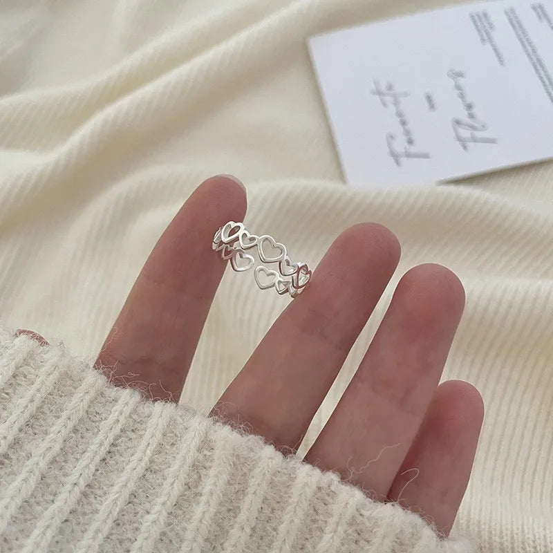 En hånd med en delikat sterling sølv justerbar ring med hul linje design mod en cremefarvet strikket baggrund.
